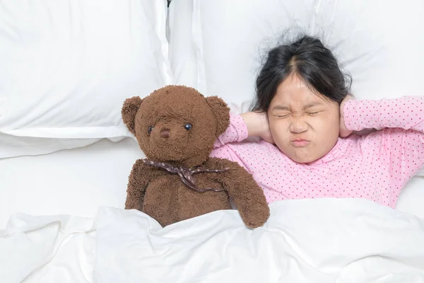 Little girl covering ears ignoring annoying loud noise, plugs ears to avoid hearing sound on bed. Health care concept