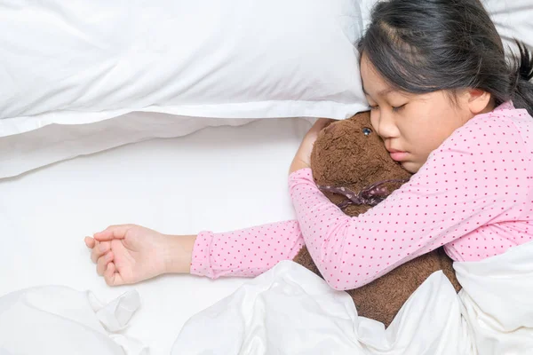 可爱的小女孩抱着一只泰迪熊 睡在自己家里的床上 享受着休息和医疗保健的理念 — 图库照片