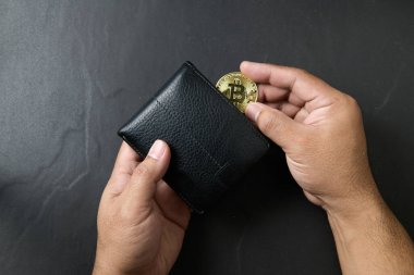 İş adamı siyah arka planda siyah deri bir cüzdana bitcoin koymuş. Bitcoin konseptini kurtarmak. İnternet bankacılığı ve uluslararası ağ ödemeleri için elektronik sanal para,