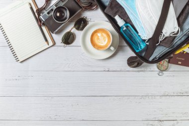 Prepare mask and alcohol spray in suitcase, vintage camera, notebook, map  on white wood and copy space. travel and prevent covid 19 concept