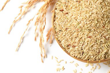 Pişmemiş kahverengi pirinç taneleriyle dolu geleneksel dokuma sepetinin üst görüntüsü izole edilmiş. Altın pirinç sapları ve gevşek taneler beyaz arka planda sepetin etrafına sanatsal olarak saçılmıştır.