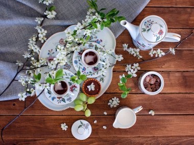 Beyaz çiçekli fincanlarda kahve ve ahşap masada çaydanlık.