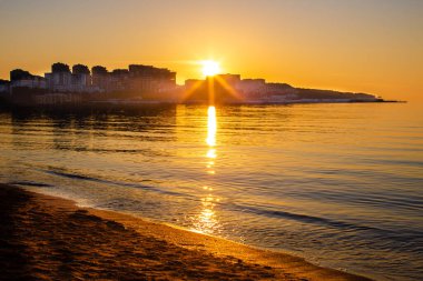Gün batımında güneş ışığı şehrin üzerinde denizin üzerinde.
