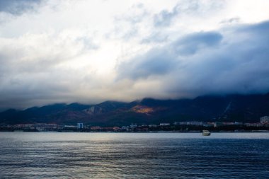 Deniz kenarındaki dağlara ve bulutlara bak.