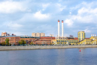 Nehrin diğer tarafındaki binalar ve bacalar görünüyor.