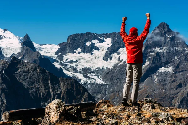 山の上に赤いジャケットを着た男 リアビュー 観光客は山の上に立って 何が起こっているかを楽しんでいます アクティブスポーツの概念 その男は山の頂上に着いた スペースのコピー — ストック写真