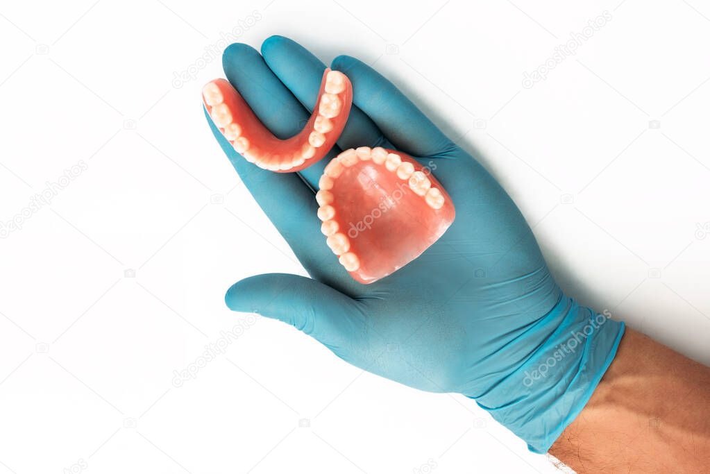 The doctor's hand in a blue glove holds a denture. Dental prosthesis in the hands of the doctor close-up. Dentist holding ceramic dental bridge. Dentistry conceptual photo. Prosthetic dentistry.