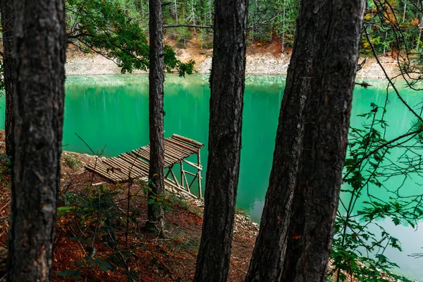 Forest lake with wooden pier. Beautiful turquoise lake with a wooden pier in a coniferous forest. Emerald forest lake. Landscape photography. Copy space