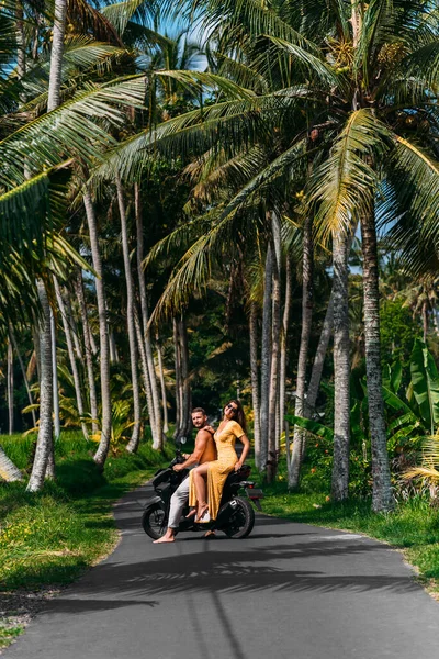 A couple in love on a scooter among the palm trees. Happy couple on vacation in Bali. The couple travels the world. Vacation in Asia. Traveling on a scooter in Bali. Honeymoon trip. Vacation in Bali