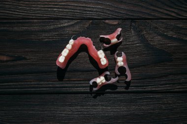 Koyu bir arka planda takma dişler. Takma dişlerin yakın plan çekimi. Dişçilik kavramsal fotoğrafçılıktır. Protez dişçilik. Takma diş. Protezler. Plastik protezlere yakın çekim. Ahşap arkaplanda dişler