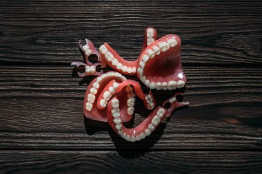 Koyu bir arka planda takma dişler. Takma dişlerin yakın plan çekimi. Dişçilik kavramsal fotoğrafçılıktır. Protez dişçilik. Takma diş. Protezler. Plastik protezlere yakın çekim. Ahşap arkaplanda dişler