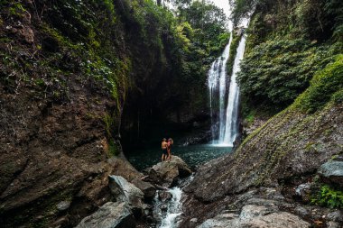Bir adam şelalede bir kadını kollarında tutuyor. Şelaledeki çift, dikiz manzaralı. Balayı gezisi. Bali 'de tatilde olan mutlu çift. Aşık bir çift dünyayı gezer. Boşluğu kopyala
