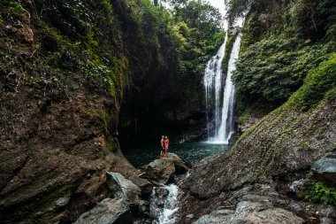 Şelalede bir adam güzel bir kadının elini tutuyor. Şelalede aşık bir çift. Balayı gezisi. Bali adasında mutlu bir çift. Güzel bir çift dünyayı gezer. Endonezya 'ya Seyahat