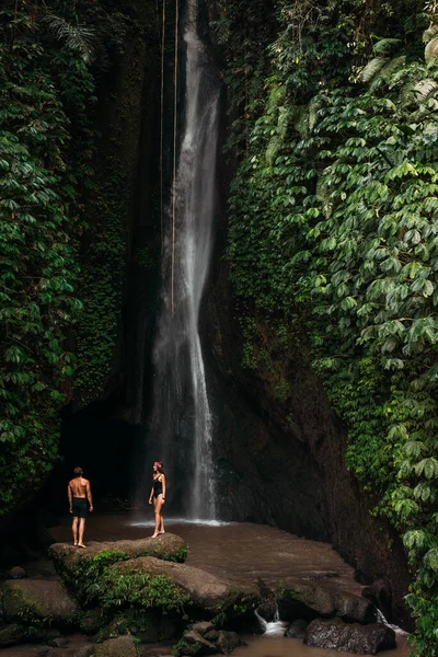Couple at a tropical waterfall. The couple travels to the island of Bali in Indonesia. A woman and a man at a beautiful waterfall. Vacation on a tropical island. Traveling couple at the waterfall