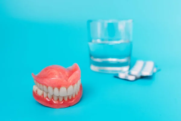 A prosthesis and a glass with a solution. Dental prosthesis care. Full removable plastic denture of the jaws. Upper and lower jaws with artificial teeth. Dentures or false teeth close-up. Copy space