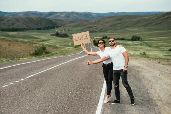 美しいカップルはヒッチハイクです 男と女が道路で投票している 夫婦は輸送を止めようとする 人々は一人で旅行する 全国各地を旅する 国内観光 — ストック写真