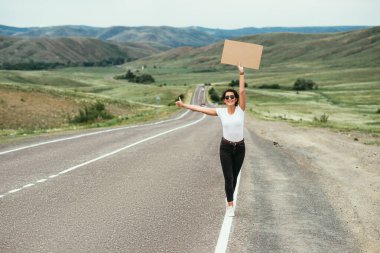 Kız otostop çekiyor. Bir kadın yolda otostop çekiyor. Kırsal bir yolda otostop çekerek. Seyahat ve otostop konsepti. Güzel kız gezgin. Boşluğu kopyala