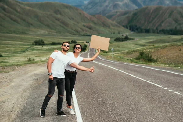 若い夫婦が道路に投票している 幸せなカップルヒッチハイクと道路上の標識と投票 幸せな男性と女性のバックパッカーのハイカーが一緒に 道路上で投票旅行 スペースのコピー — ストック写真