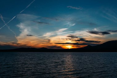 Gün batımında güzel bir dağ gölü. Gün batımında dağların arasında bir göl. Akşam manzarası. Gün batımında karanlık bulutlar ve siluet dağ aynalarıyla gölde altın çağda suyun üzerinde.