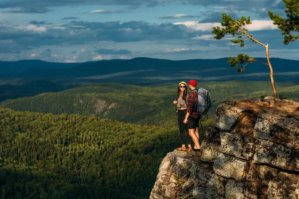 身穿旅游服的一男一女正站在岩石上欣赏着全景 两个背著背包的游客从山顶欣赏日落美景 背包客 — 图库照片