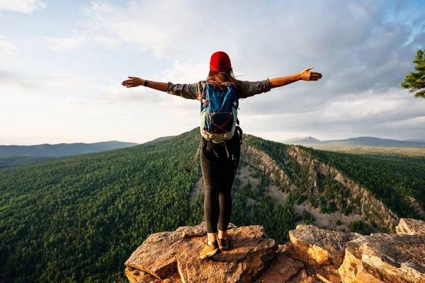 バックパックを持つ旅行者の女の子は 山の端には リアビューに立っている 崖の端に立って手を上げて空を見ている若い女性 — ストック写真
