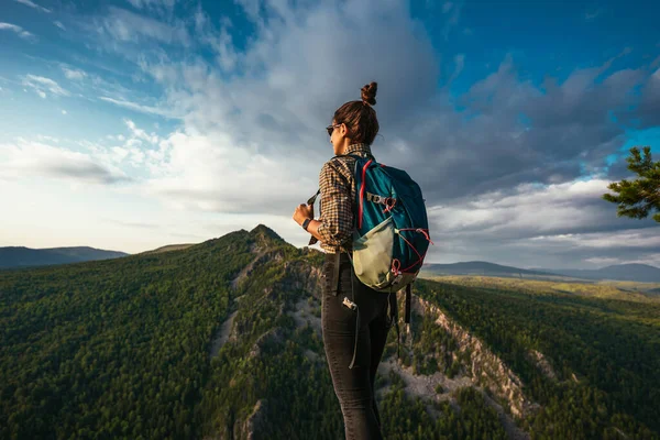 バックパック付きの若い観光客の女の子は山の頂上からの夕日を楽しんでいます 山の背景に旅行者 山頂にはリュックを背負った観光客が立っている — ストック写真