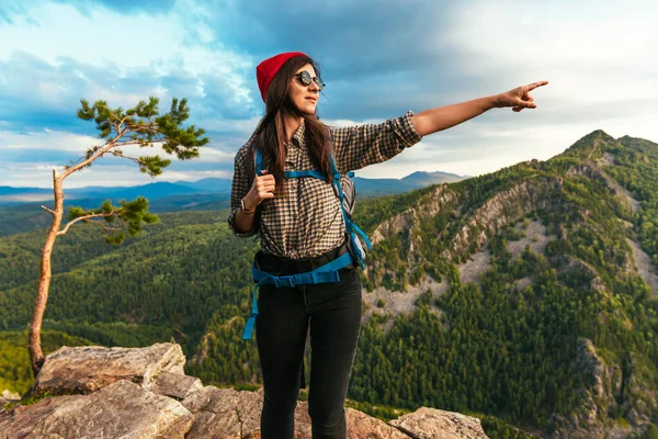 ハイキングのコンセプト 山の中の岩に沿って歩くサングラスやバックパックの観光客は 笑顔と彼女の前で何かを指しています 山の中をハイキング — ストック写真