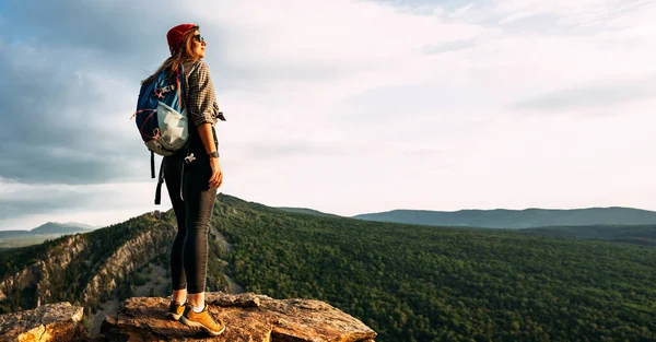 バックパック付きの若い女性観光客は パノラマの上から夕日を賞賛します 山の背景に旅行者 山を背景にバックパック付きの観光客 — ストック写真