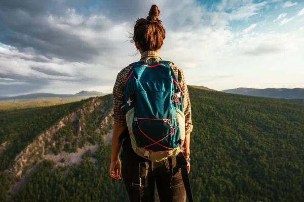 リュックを背負った観光客の女の子は山の頂上からの夕日を賞賛しています 山の背景に旅行者 山の頂上にはリュックを背負った観光客が立っている — ストック写真