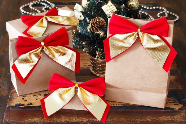Gifts paper package with red golden bow near small Christmas tre — Stock Photo, Image