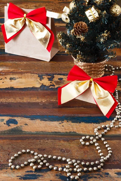 Paquete de regalos con lazo rojo dorado cerca de un pequeño árbol de Navidad —  Fotos de Stock