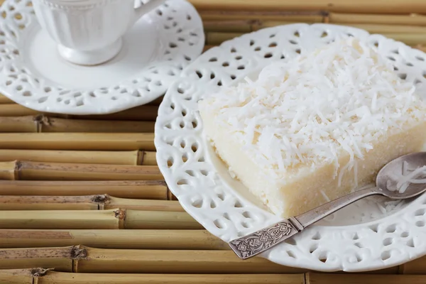 Zoete couscous pudding (cuscuz doce) kokosnoot op vintage plaat, kopje koffie op bamboe bord. — Stockfoto