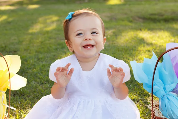 Cute little baby girl in white dress near wicker basket with gifts in park — Stock Photo, Image