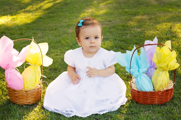 Cute little baby girl with wicker basket with chocolate eggs — Stock Photo, Image