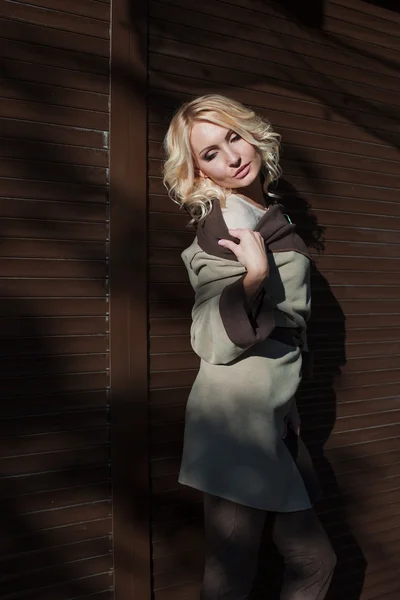Красивая блондинка в пальто стоит у стены — стоковое фото
