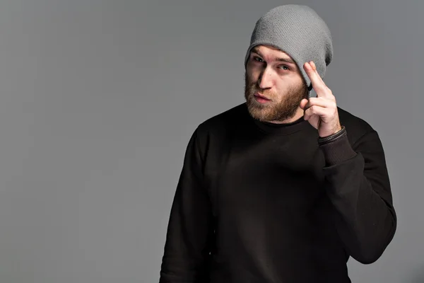 A young man with a beard wearing a hat on a gray background — Stock Photo, Image