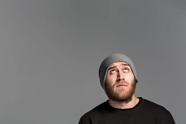 Un giovane con la barba che indossa un cappello su sfondo grigio — Foto Stock