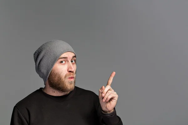 Молодой человек с бородой в шляпе на сером фоне — стоковое фото