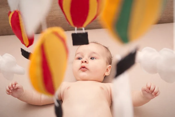 Söpö rotujenvälinen vauva katsomassa hänen ilmapallo mobiili kun makaa hänen pinnasänky — kuvapankkivalokuva