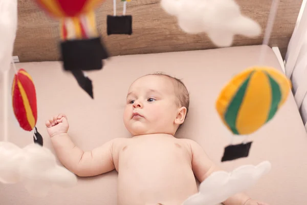 Lindo interracial bebé viendo su globo móvil mientras yacía en su cuna —  Fotos de Stock