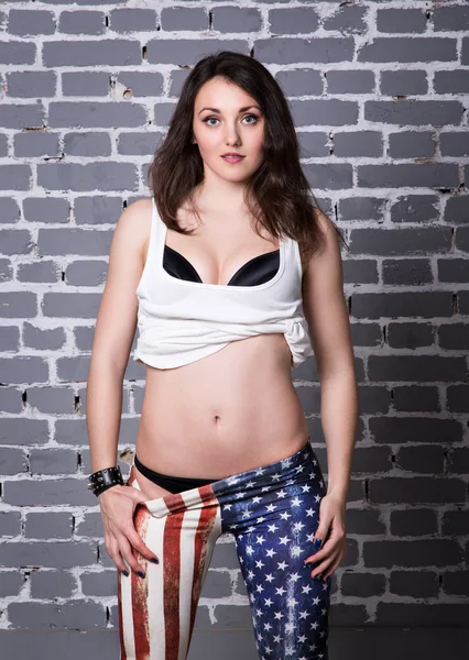 Beautiful girl in white shirt in black bra in American flag pants with black hair posing. — Stock Photo, Image
