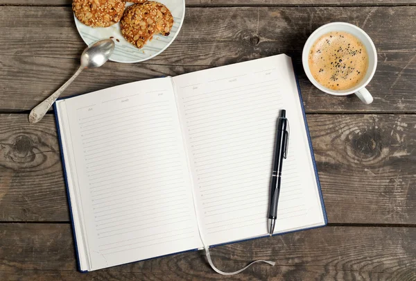 Diary with a pen, coffee and saucer with cookies on a wooden ta — стоковое фото