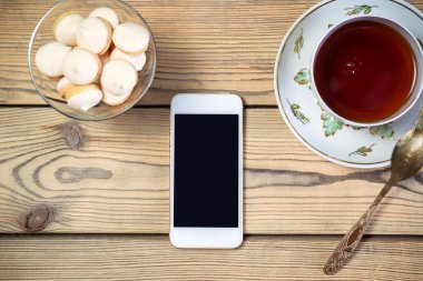 Aperatif ve ahşap masa üstünde hareket eden telefon ile çay