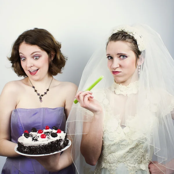 Bride trying to diet and eating celery is tempted by bridesmaid holding up cake — Stock Photo, Image