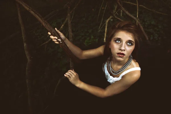 Young woman lost in the dark woods wearing a necklace and white blouse