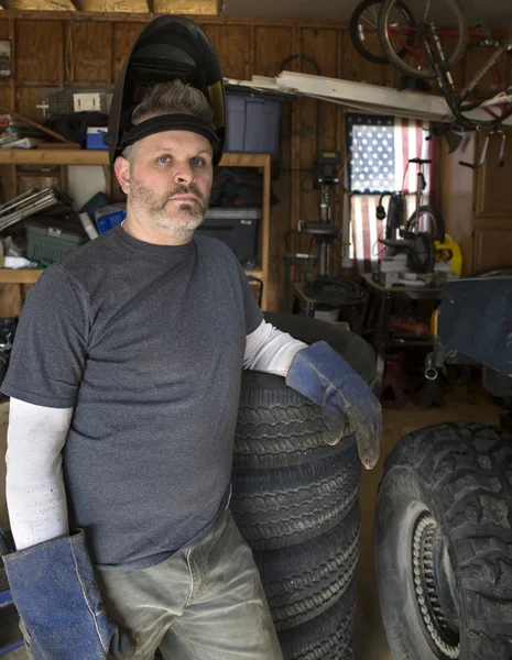 Man wearing welding helmet leaning against tire — Stock Photo, Image