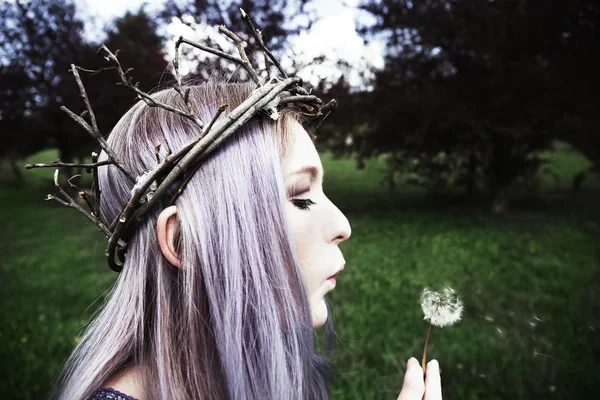 Young woman wearing twig crown and blowing on dandelion — Stock Photo, Image