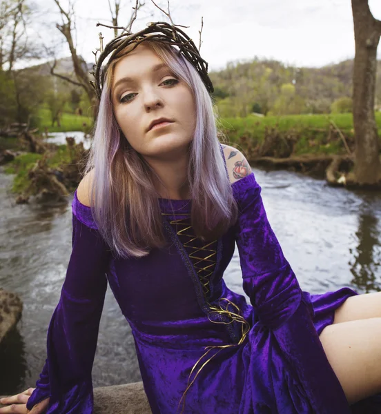 Jovem mulher de vestido roxo sentado junto a um rio — Fotografia de Stock