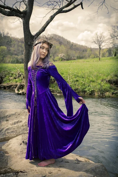 紫のガウンに川のそばに立っている若い女性. ストックフォト