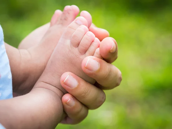 Mãe segurando pés de bebê com fundo natural — Fotografia de Stock